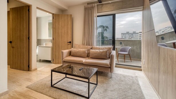 Ein modernes Wohnzimmer mit Sofa, Couchtisch und Blick auf die Stadt durch große Fenster.