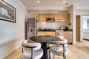 Una cocina moderna con armarios de madera, un refrigerador, una estufa y un comedor con mesa de mármol y sillas acolchadas.