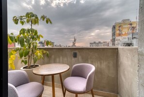 Ein Balkon mit rundem Tisch, zwei Stühlen, einem Blumentopf und Blick auf die Stadt.