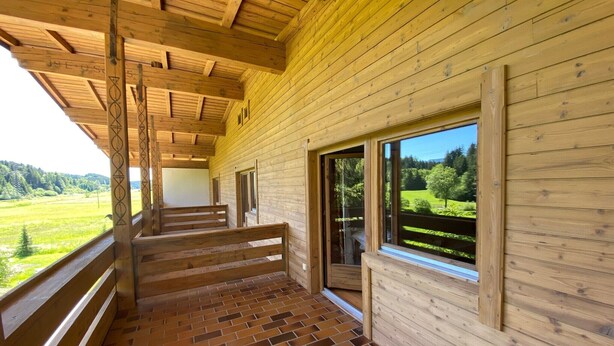 En træhytte med balkon, murstensgulv og udsigt over et grønt landskab.