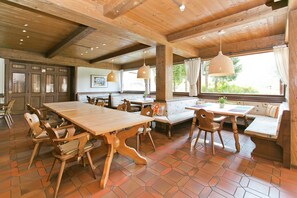 Un interior de fusta amb una taula gran de dinar, cadires i una banca amb coixins.