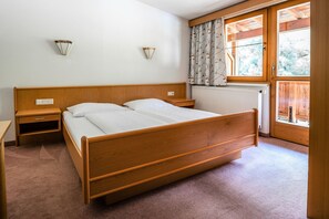 A bedroom with a wooden bed, two bedside tables, a radiator, and a window with curtains. - Chalet in Angerberg for groups (Angerberg)