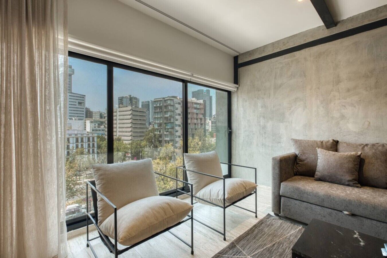 A modern living room with a large window, a sofa, and two armchairs.