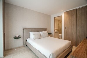 A bedroom with a bed, bedside tables, a nightstand, a wooden wardrobe, and a bathroom visible through an open door. - Casa Monroy - 1BR en Roma Norte - LowF (Mexico City)