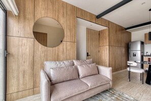 A modern living room with a sofa, a round mirror, and a kitchen area with a refrigerator. - Myla 01 - 1BR - In Roma Norte H (Mexico City)