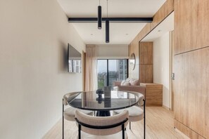 A modern living room with a glass dining table, a sofa, and a TV mounted on the wall. - Myla 01 - 1BR - In Roma Norte H (Mexico City)