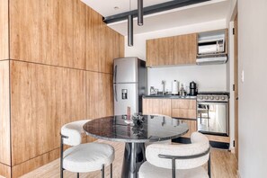 A modern kitchen with wooden cabinets, a round marble table, and a built-in oven. - Myla 01 - 1BR - In Roma Norte H (Mexico City)