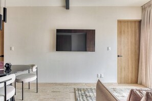 A modern living room with a flat-screen TV mounted on the wall, a dining area with a round table and chairs, and a wooden door. - Myla 01 - 1BR - In Roma Norte H (Mexico City)