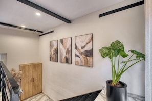 A hallway with a wooden cabinet, abstract wall art, and a potted plant. - Myla 04C - 1BR In Roma Norte - HighF (Mexico City)