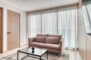 A modern living room with a sofa, a coffee table, and a large window with sheer curtains. - Myla 04C - 1BR In Roma Norte - HighF (Mexico City)