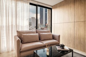 Ein modernes Wohnzimmer mit einer Couch, einem Glastisch und Blick auf eine Stadtlandschaft durch große Fenster.