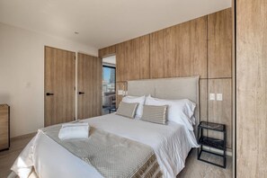 A bedroom with a large bed, wooden panel walls, a small side table, and a view of the city through a door. - Myla 04C - 2BR In Roma Norte - HighF (Mexico City)
