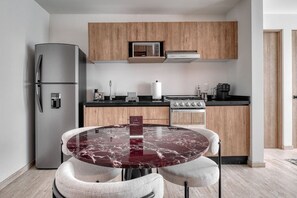 A compact kitchen with a refrigerator, microwave, stove, and wooden cabinets. - Myla 04C - 2BR In Roma Norte - HighF (Mexico City)