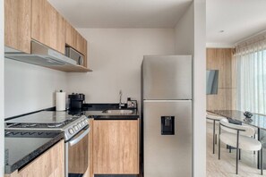 Eine moderne Küche mit Herd, Backofen und Kühlschrank, Holzsärchen und einer Essecke mit Tisch und Stühlen.