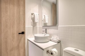 Ein Badezimmer mit weißem Waschbecken, einem Spiegel, einer Toilette und einer Holztür.