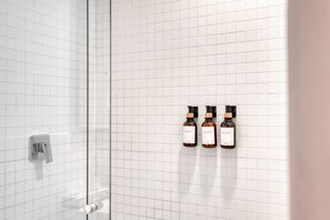 A bathroom with white tiled walls, a glass shower door, and three bottles of shampoo, conditioner, and body wash on the wall. - Superior 2 BR near Reforma (Mexico City)
