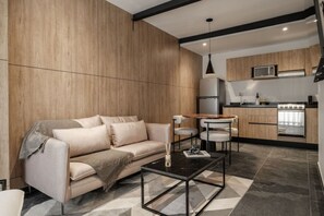 A modern living room with a sofa, coffee table, and dining area, connected to a kitchen with appliances and wooden cabinetry. - Elegant 1BR near Reforma, LowF (Mexico City)