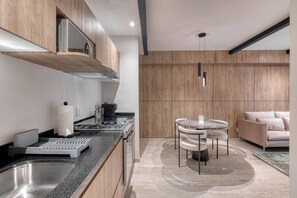 A modern kitchen with a stainless steel sink, a stove, and wooden cabinets. There is a round table with chairs in the dining area, and a sofa in the living area. - Elegant 1BR near Reforma, LowF (Mexico City)