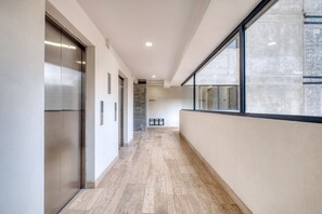 A modern hallway with elevators, a clear view through a large window, and a sign indicating room number 402 C. - Casa Herrera - in Roma Norte - LowF (Mexico City)