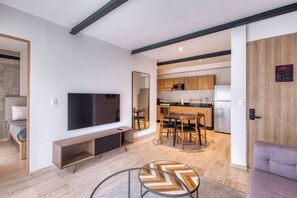Ein modernes Wohnzimmer mit Flachbildfernseher, einer Holz-Unterhaltungseinheit, einem Essbereich mit Tisch und Stühlen sowie einer Küche mit Holzausstattung und Geräten.