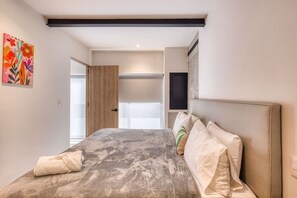 Ein Schlafzimmer mit Bett, Kissen, Kopfteil, einer Tür und einem an der Wand befestigten Fernseher.