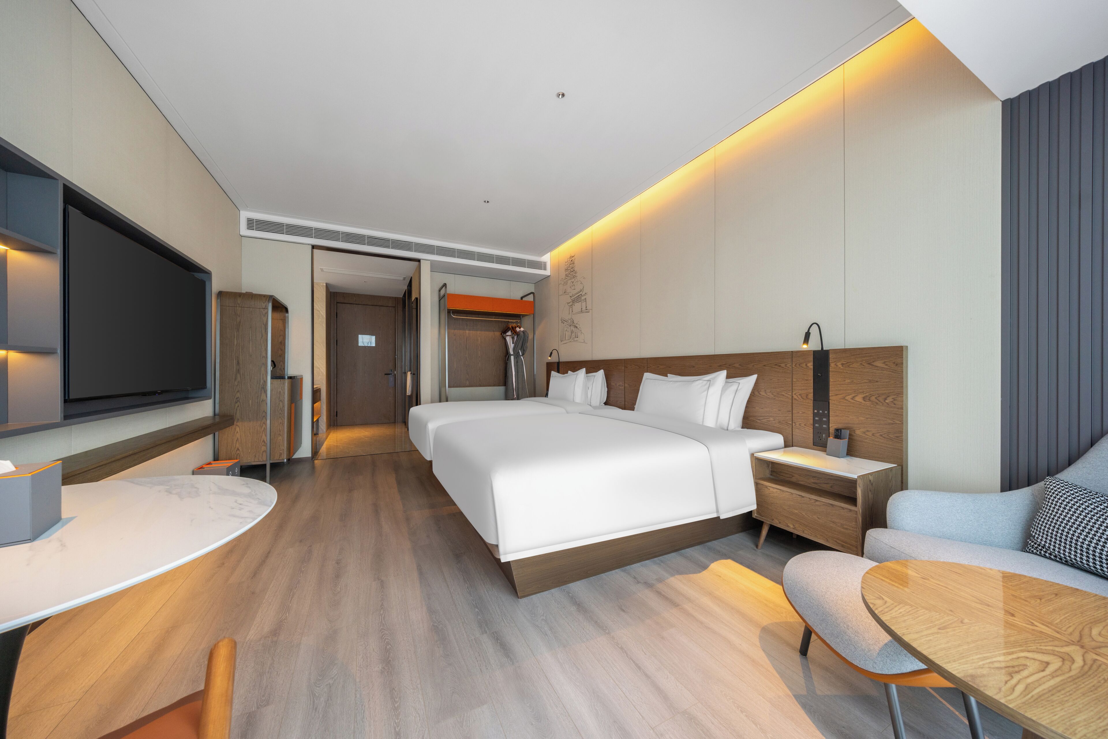 A modern hotel room with a large bed, a desk, a TV, and a seating area.