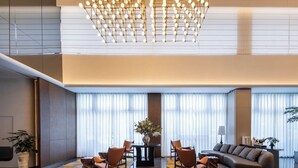 Una hall moderna di un hotel con un lampadario, un'area salotto e ampie finestre.