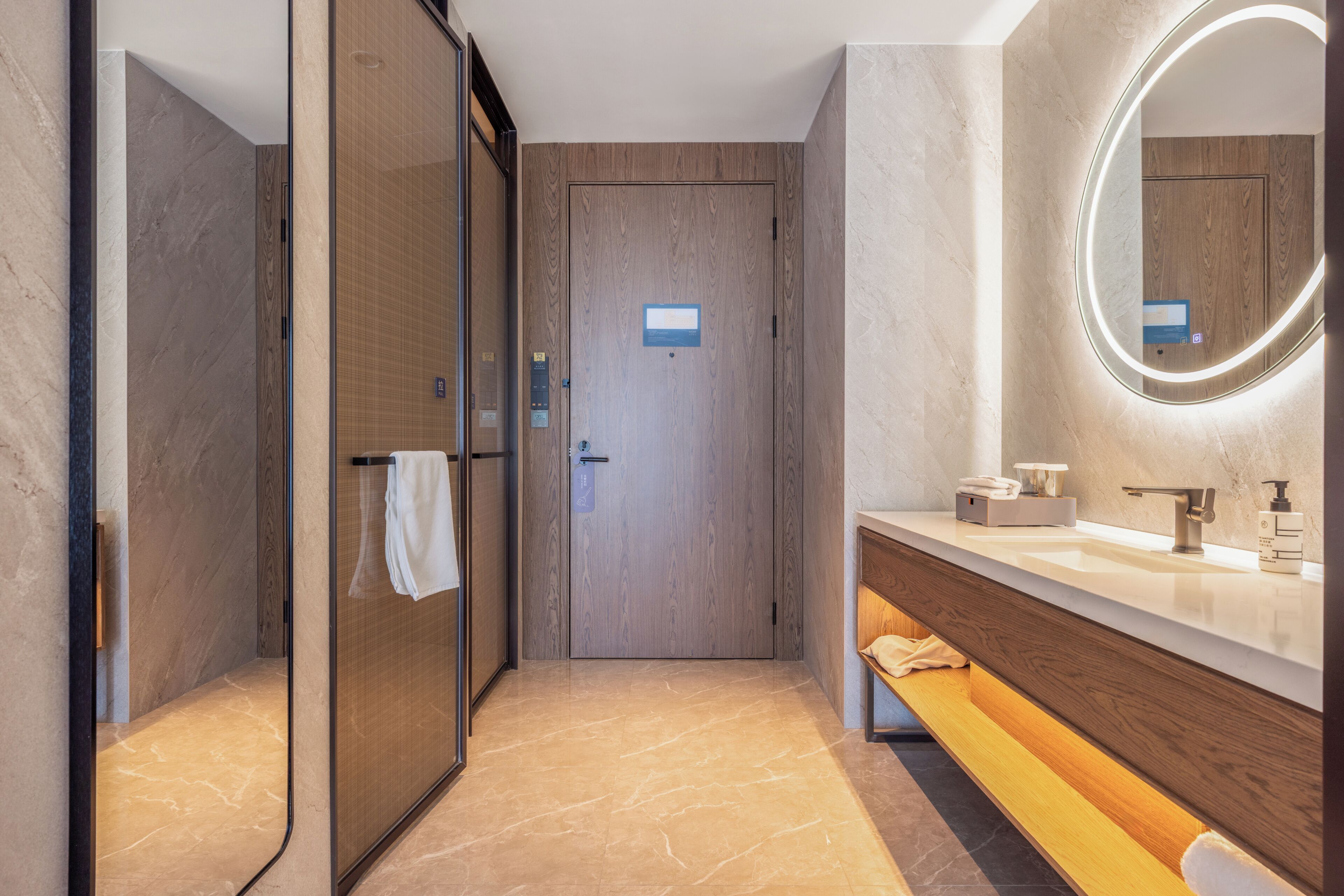 A modern bathroom with a glass shower enclosure, a wooden vanity, a mirror with a light, and a bench.