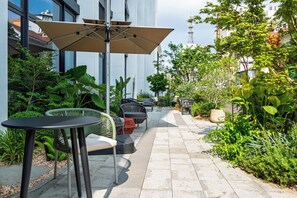 An outdoor seating area with tables and chairs, surrounded by greenery and a building in the background. - UrCove by Hyatt Nanjing South Railway Station BaiJia Lake (Nanjing)