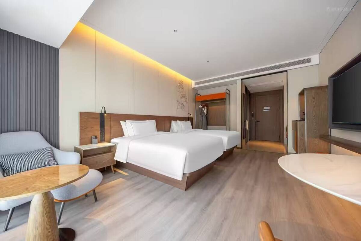 A hotel room with a bed, bedside tables, a desk, a chair, a TV, and a wardrobe.
