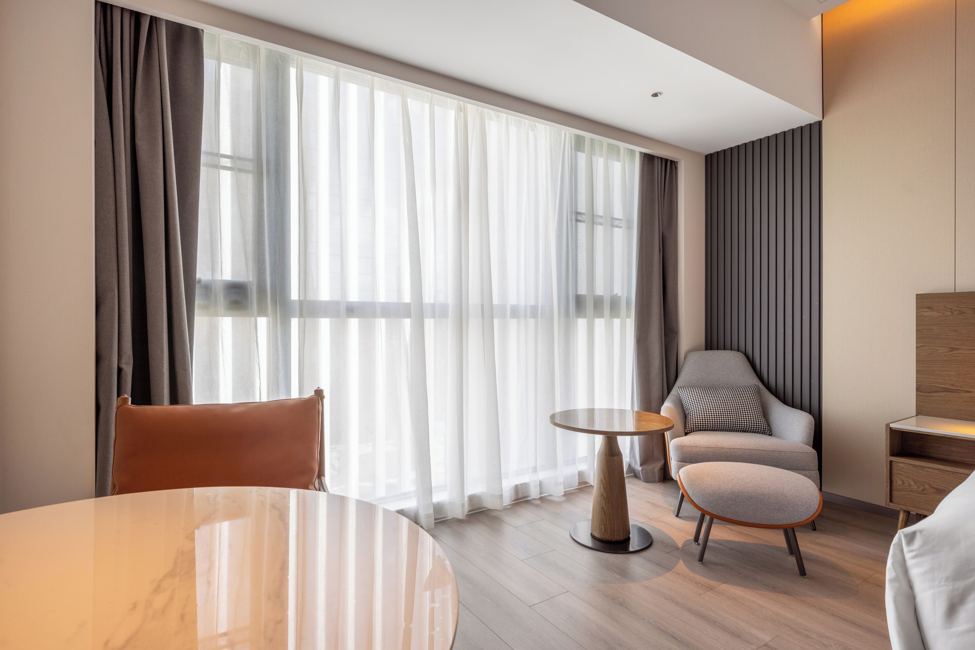 Ein modernes Hotelzimmer mit einem runden Marmortisch, einer Couch, einem Sessel und einem kleinen Beistelltisch.