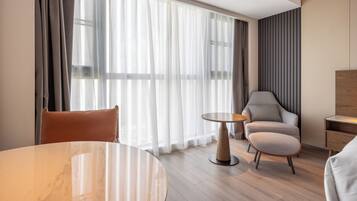 Ein modernes Hotelzimmer mit einem runden Marmortisch, einer Couch, einem Sessel und einem kleinen Beistelltisch.