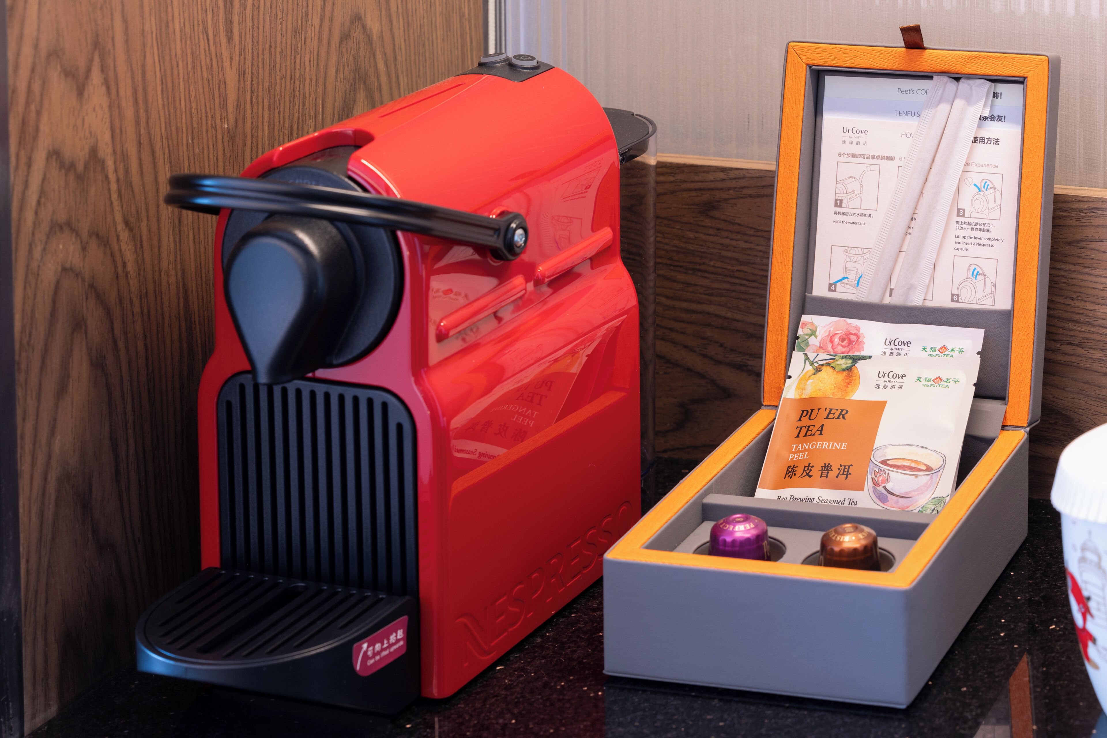 A red coffee machine with a manual in a box beside it.
