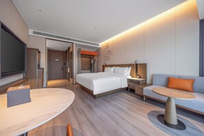Quarto de hotel com cama, sofá, televisão e mesa.