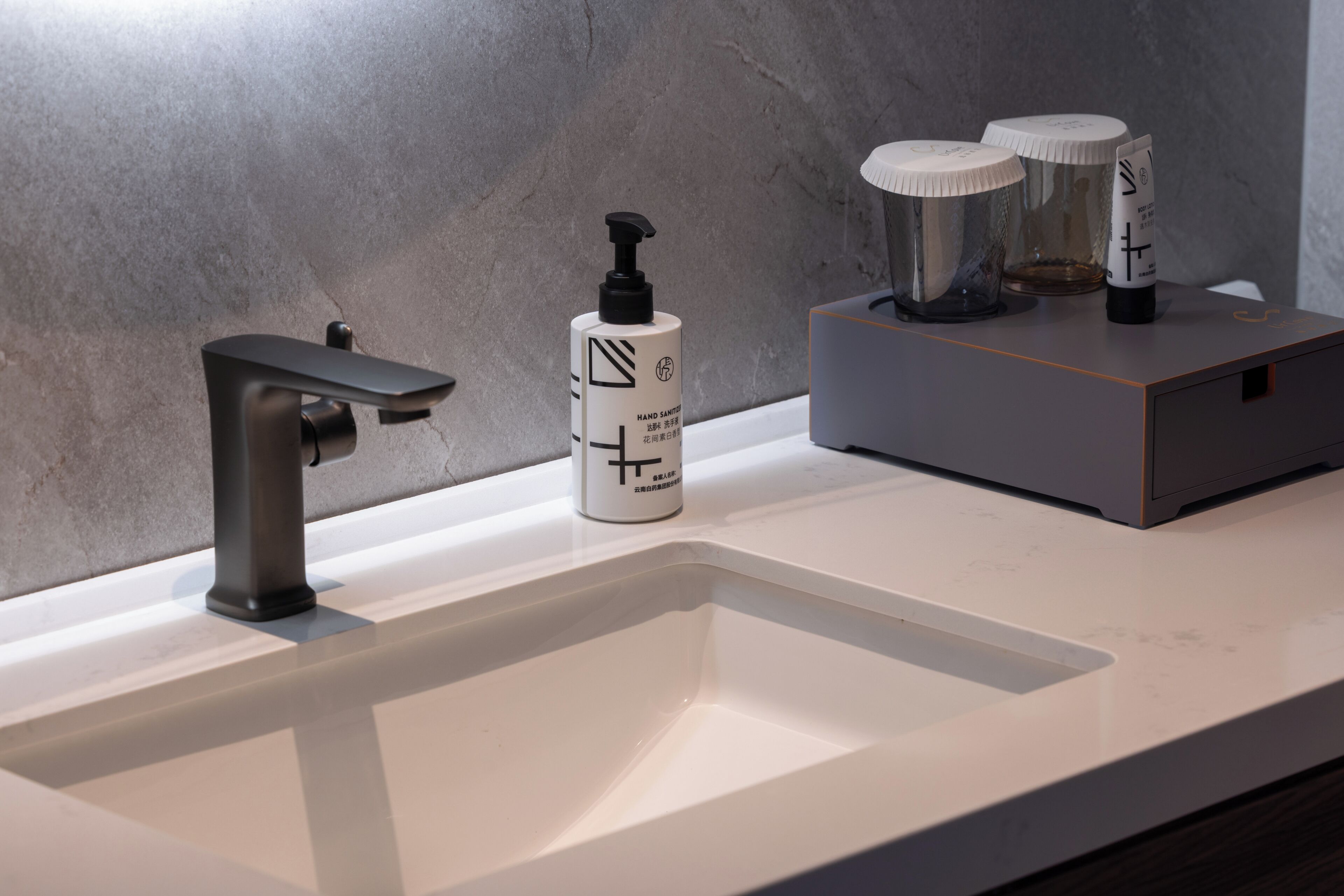 Une salle de bain moderne avec un robinet élégant, un distributeur de gel hydroalcoolique et un distributeur de savon, le tout posé sur un comptoir en marbre.