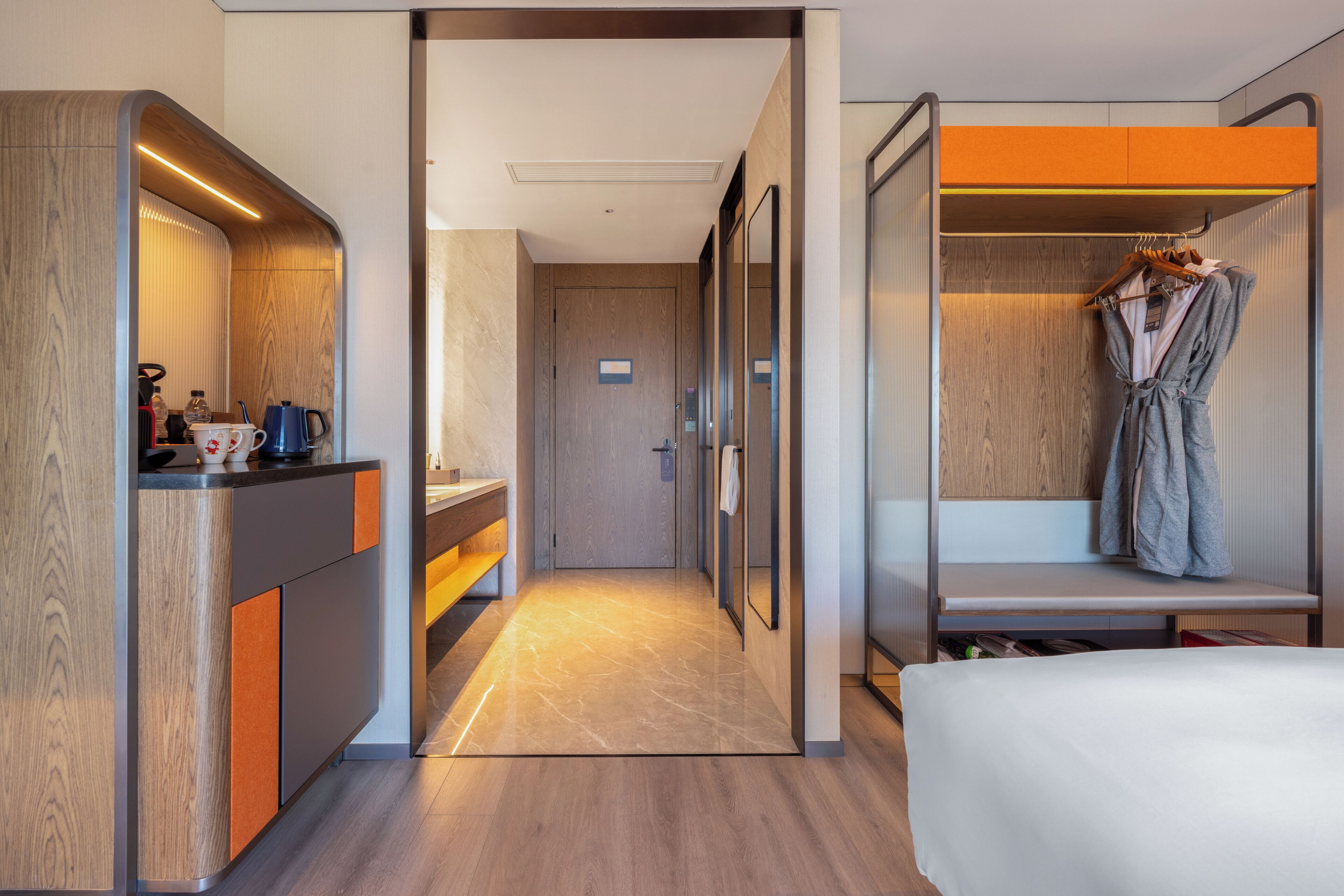 A hotel room with a wooden vanity, a robe hanging on a rack, and a bed.
