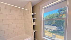 Une salle de bain avec une baignoire, une fenêtre donnant sur une forêt et une serviette accrochée au bord de la baignoire.