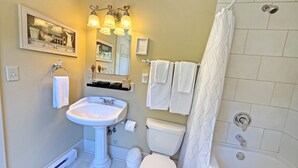 Une salle de bain comprenant un lavabo sur colonne, des toilettes, une douche et un miroir au-dessus du lavabo.