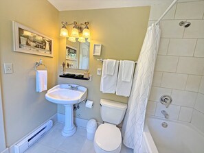 Baño con lavamanos pedestal, inodoro, ducha y espejo sobre el lavamanos.