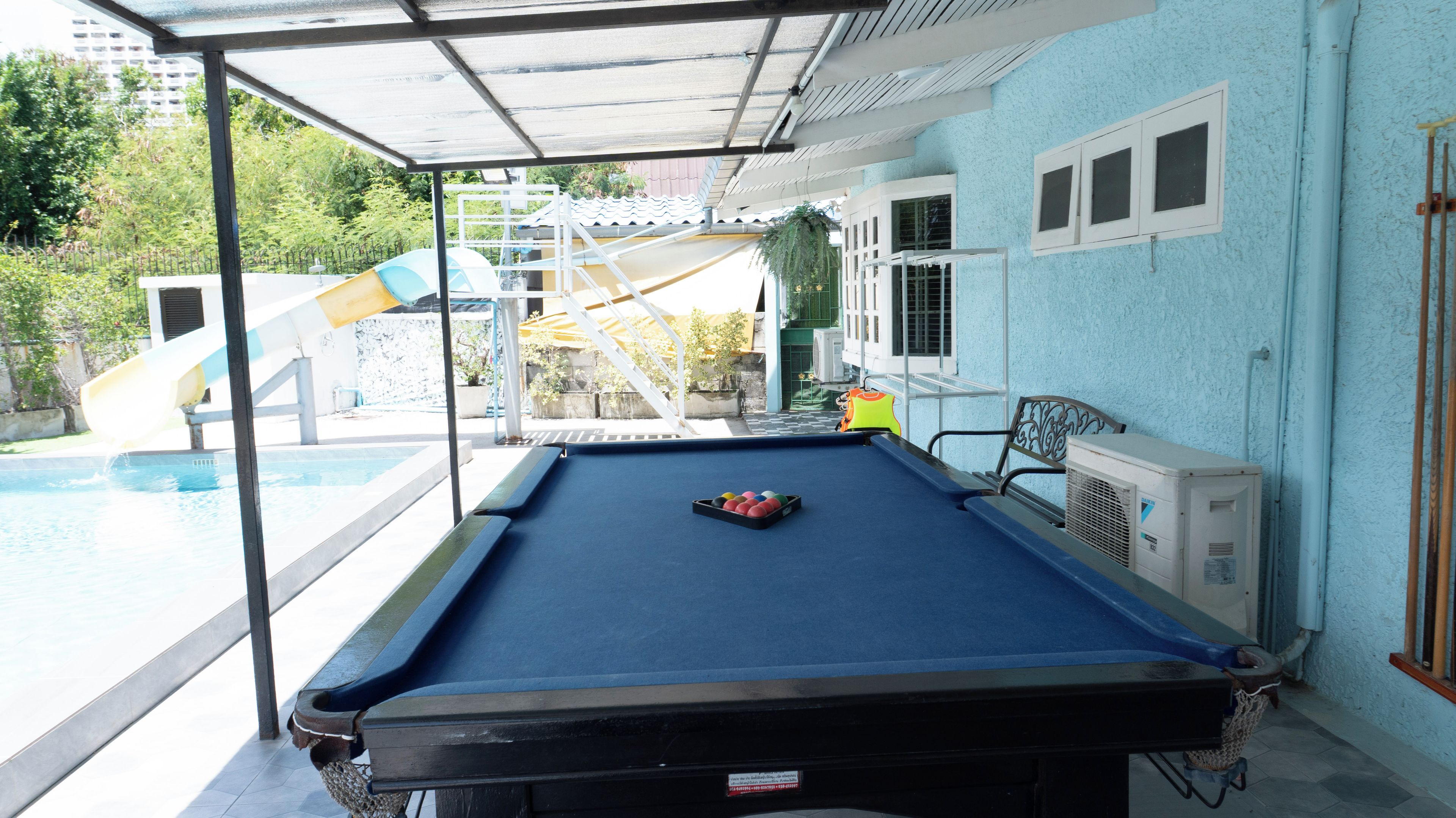 A pool table with a blue felt surface, a water slide in the background, and a building with light blue walls.