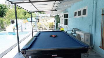 A pool table with a blue felt surface, a water slide in the background, and a building with light blue walls.