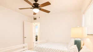 A bedroom with two beds, a ceiling fan, a nightstand with a lamp, and a door leading to another room.