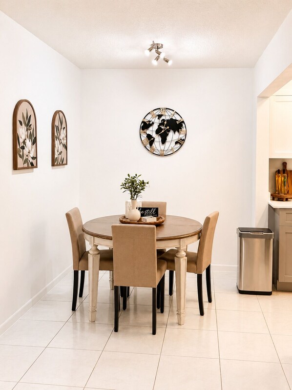 A dining area with a round table, six chairs, a world map wall decoration, two framed floral artworks, and a potted plant.