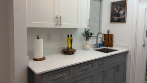 A kitchen with white upper cabinets, a gray lower cabinet, a white countertop, a stainless steel sink, and a wooden cutting board. - Apartment in Hollywood Beach, a 10-minute drive from the beach (Hollywood)