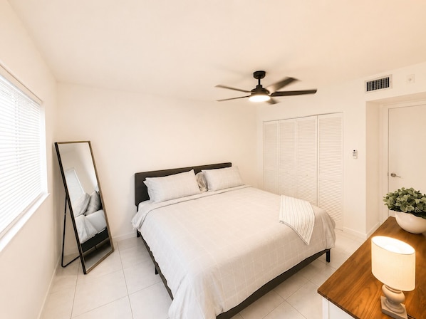 Une chambre à coucher comprenant un lit, un ventilateur de plafond, une table de chevet avec une lampe, un miroir et une armoire.
