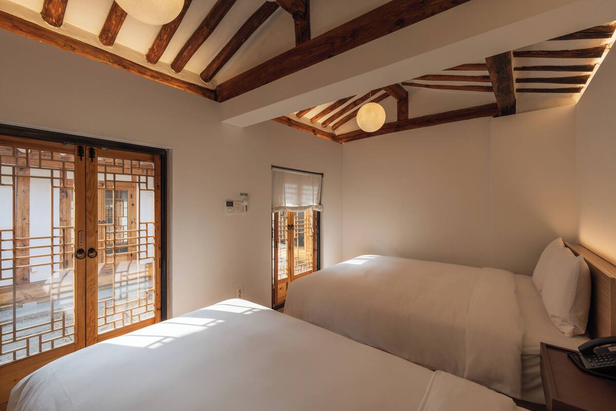 Un dormitorio con cama, vigas de madera, una ventana y una puerta de diseño tradicional.