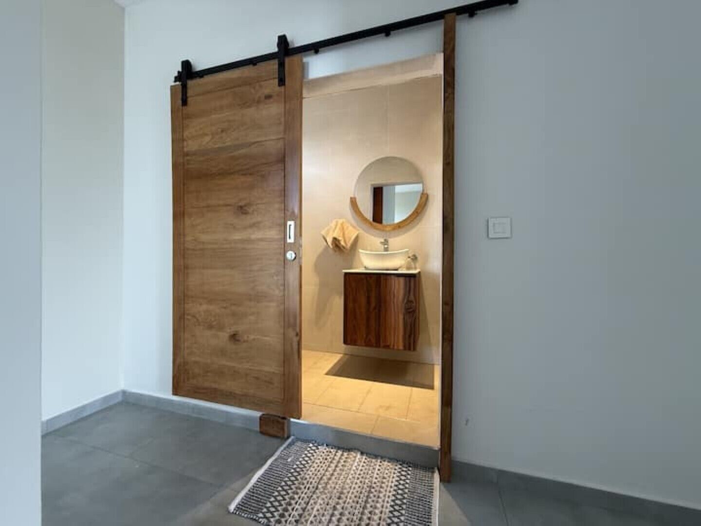A room with a sliding wooden door leading to a bathroom with a sink and mirror.