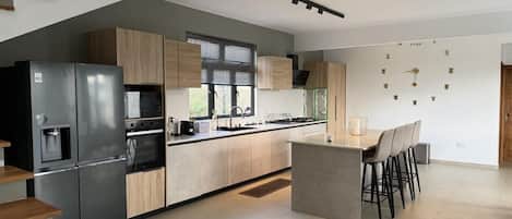 A modern kitchen with a built-in refrigerator, a stove, and a sink. There is a bar area with stools and a window with blinds.