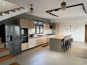 A modern kitchen with a built-in refrigerator, a stove, and a sink. There is a bar area with stools and a window with blinds. - Cozy Luxe - 4 bedrooms Villa with private pool (Mahebourg)