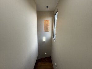 A narrow hallway with a wooden staircase, a textured hanging light fixture, and a wall-mounted light. - Cozy Luxe - 4 bedrooms Villa with private pool (Mahebourg)